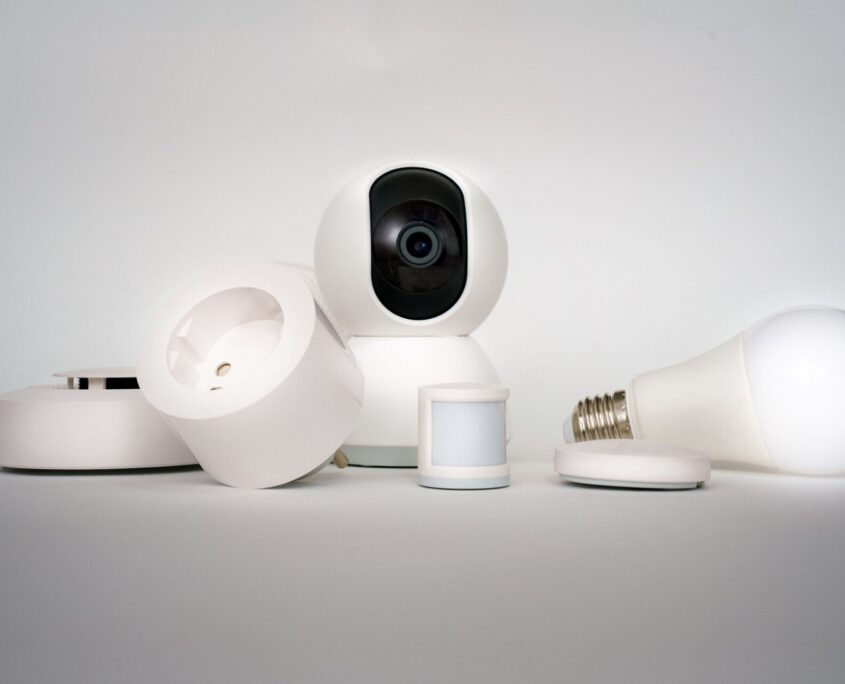 Elettrici Group - Sito Web, Gestione Social e Grafica Dispositivi di domotica smart, telecamera di sicurezza, lampadina e presa intelligente su sfondo bianco, Elettrici Group