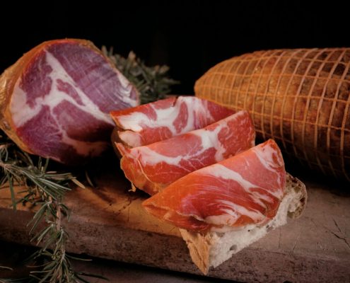 Fette di capocollo calabrese su pane casereccio con salume intero e capocollo stagionato su tagliere di legno
