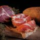 Fette di capocollo calabrese su pane casereccio con salume intero e capocollo stagionato su tagliere di legno