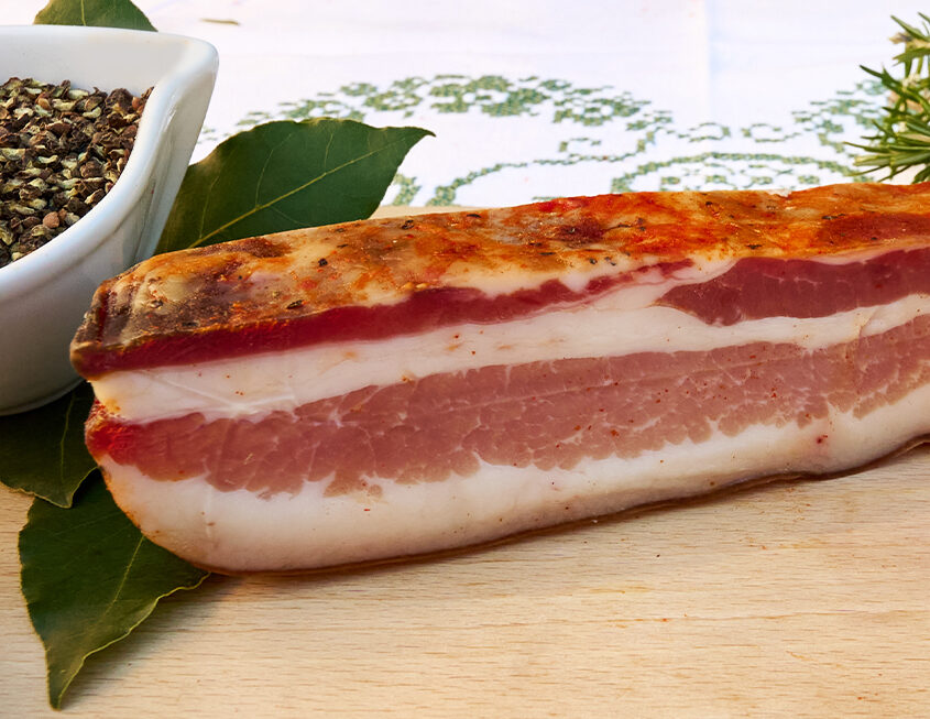 Salumificio Menotti - Prodotti Tipici, Grafica, Web e Google ADS Trancio di salume stagionato tipico con spezie e foglia di alloro su tagliere in legno, Salumificio Menotti
