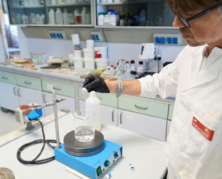 Tecnico di laboratorio in camice bianco e guanti che effettua test chimici con contagocce e becher su piastra riscaldante