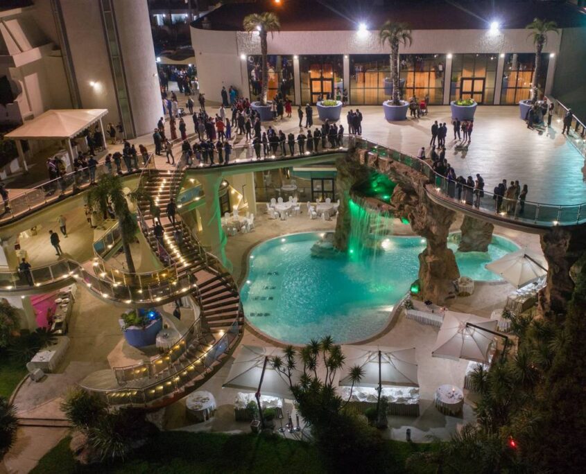 Sala Madame Lilla - Vista Notturna e Piscina - Twister ADV Catanzaro Vista panoramica notturna dall'alto di Sala Madame Lilla con piscina illuminata, cascata artificiale, scalinata scenografica e ospiti in terrazza