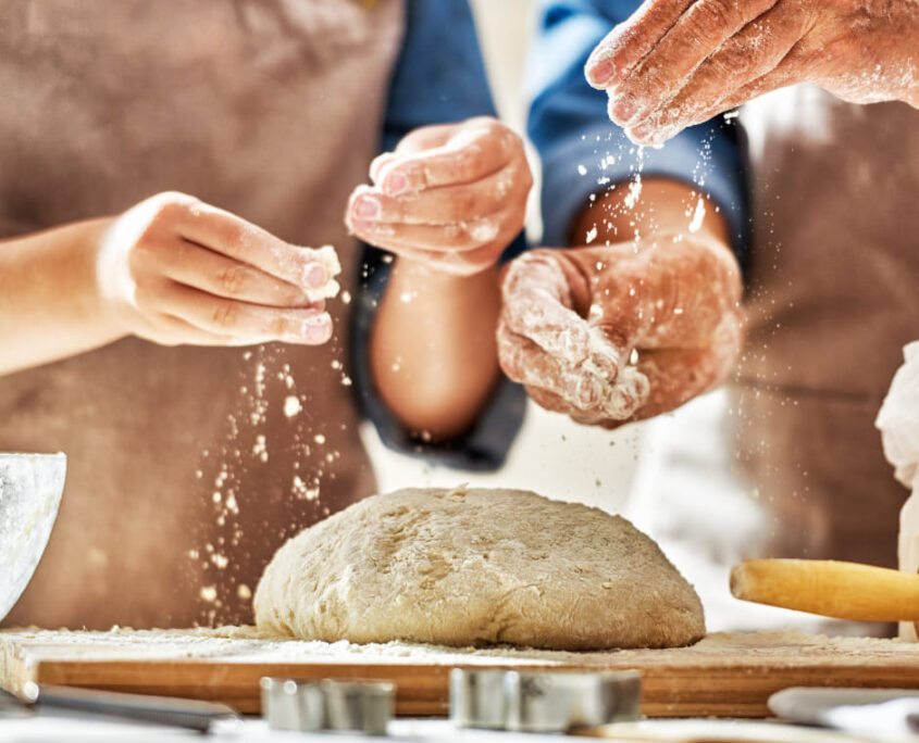 Lavorazione Artigianale dell'Impasto Fresco - Antico Forno Iuliano Twister Adv Catanzaro Mani di fornai artigiani che spolverano delicatamente la farina su un panetto di impasto fresco lavorato a mano su un tagliere in legno per Antico Forno Iuliano.