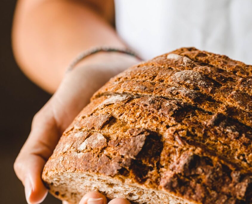 Pagnotta di Pane Casereccio Integrale Artigianale - Antico Forno Iuliano Twister Adv Catanzaro Calabria Mani che tengono con cura mezza pagnotta di pane casereccio integrale artigianale con crosta dorata e croccante per Antico Forno Iuliano.
