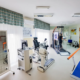 Sala di fisioterapia e riabilitazione del centro Parisan attrezzata con spalliera in legno, tapis roulant per rieducazione motoria, parallele e macchinari elettromedicali avanzati.